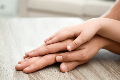 Happy family holding hands at wooden table indoors, closeup view