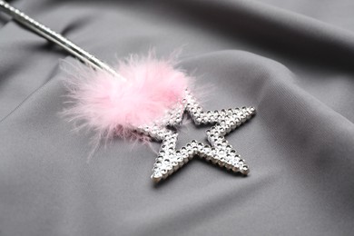 Photo of Beautiful silver magic wand with feather on grey fabric, closeup