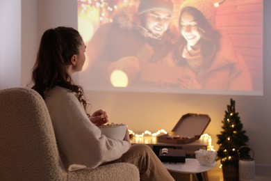 Woman with popcorn watching romantic Christmas movie via video projector at home