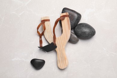 Wooden slingshot with stones on light grey marble background, flat lay