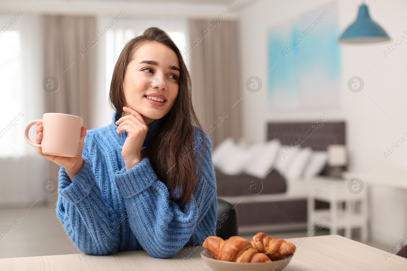 Photo of Young woman drinking coffee at table indoors. Winter season