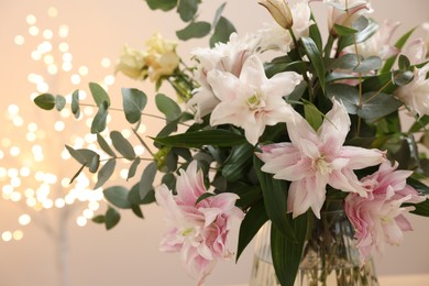 Bouquet of beautiful lily flowers in vase against beige background with blurred lights, closeup