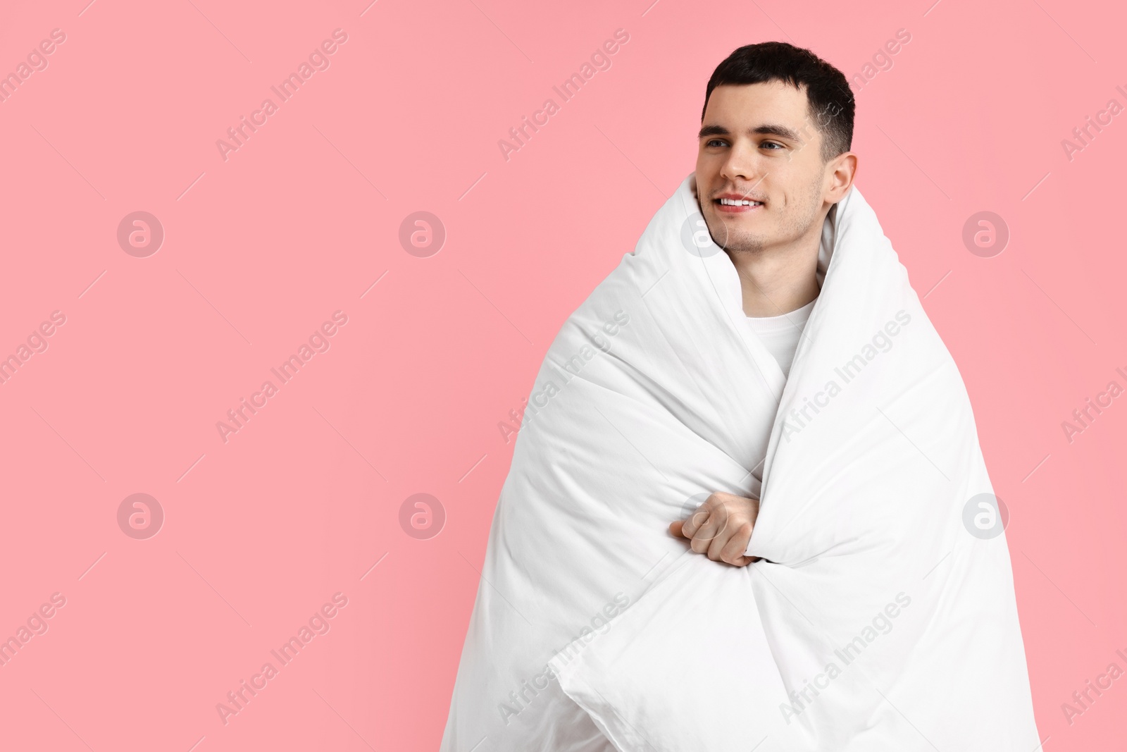 Photo of Happy man wrapped in blanket on pink background, space for text