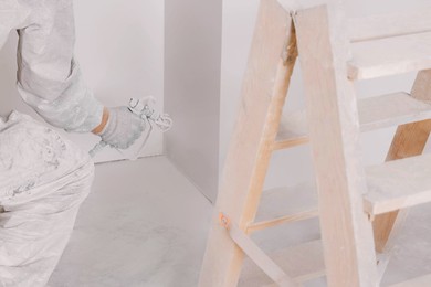 Photo of Decorator in uniform painting wall with sprayer indoors, closeup