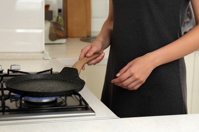 Photo of Woman putting frying pan on stove with burning gas in kitchen, closeup