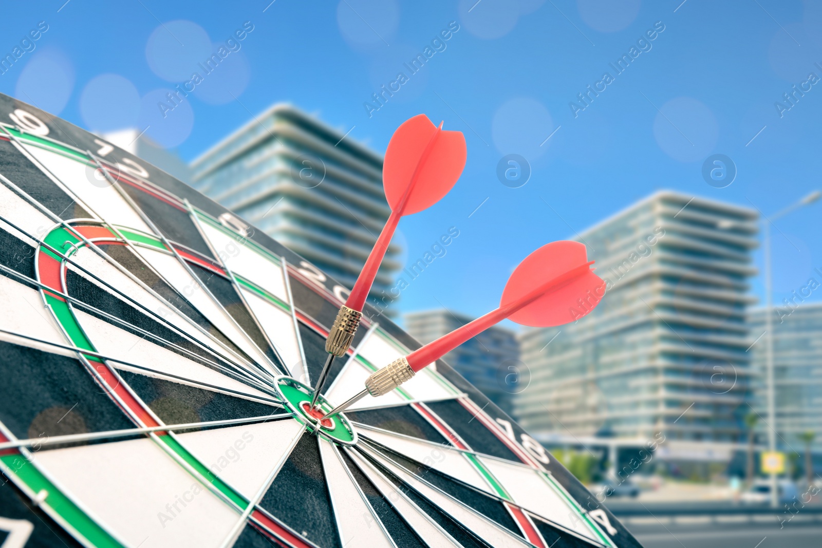 Image of Board with red darts hitting target on blurred view of cityscape