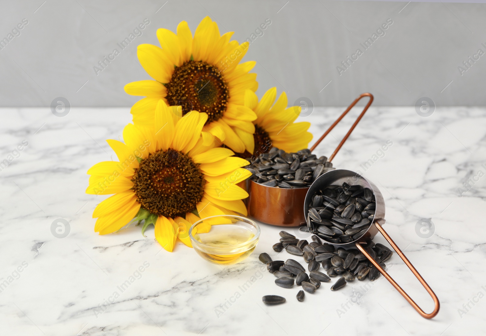 Photo of Sunflowers, oil and seeds on white marble table