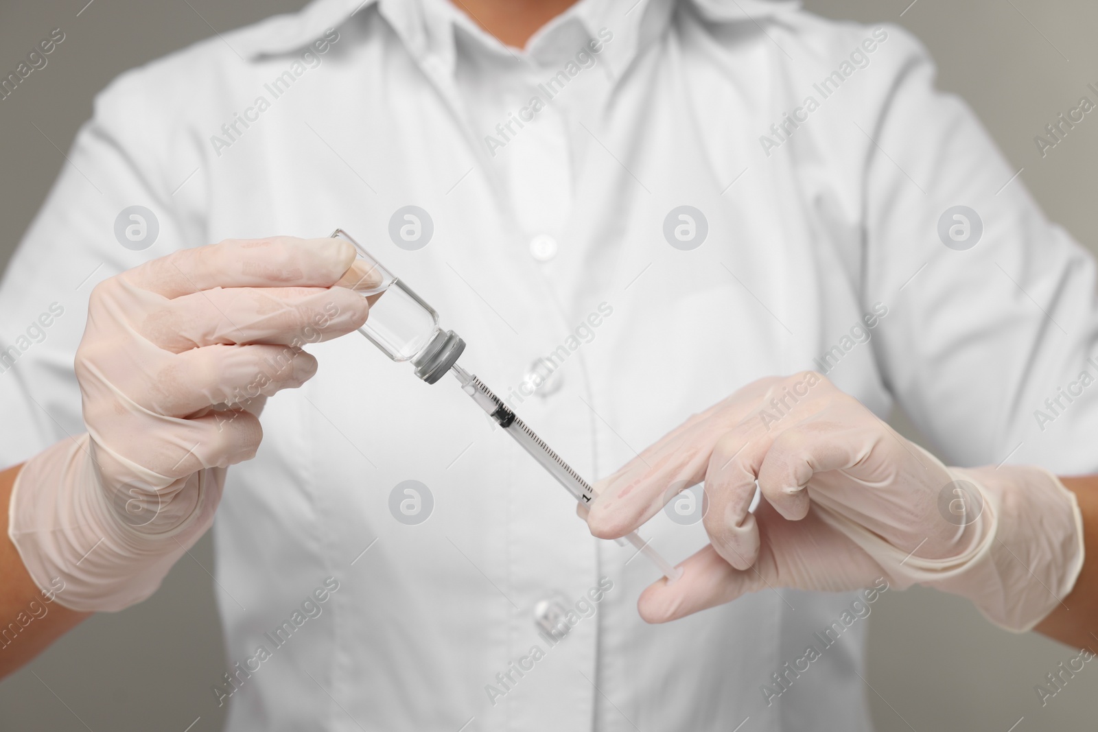 Photo of Doctor filling syringe with medication from glass vial on grey background, closeup