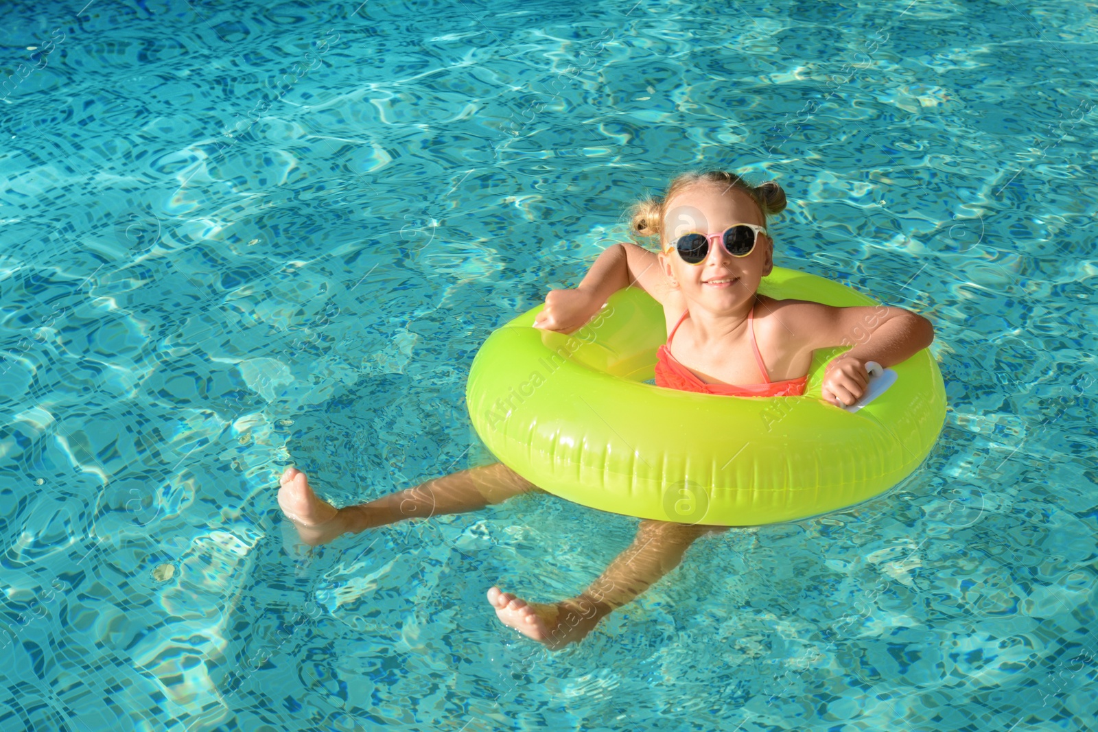 Photo of Happy little girl with inflatable ring in outdoor swimming pool on sunny day