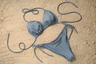 Stylish blue bikini on sand, flat lay