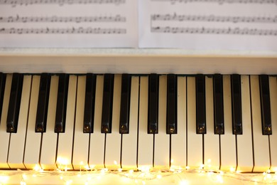 Photo of Glowing fairy lights on piano keys, above view. Christmas music