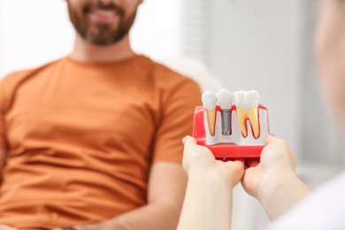 Photo of Doctor with educational model of dental implant consulting patient in clinic, closeup. Space for text
