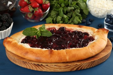 Photo of Delicious sweet cottage cheese pastry with cherry jam and fresh berries on blue wooden table, closeup