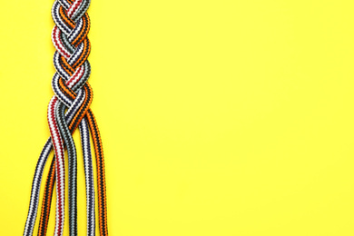 Top view of braided colorful ropes on yellow background, space for text. Unity concept