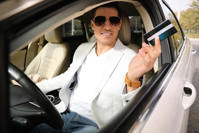 Photo of Man sitting in car and giving credit card at gas station