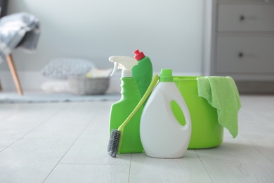 Photo of Bucket with cleaning products and supplies on floor indoors. Space for text