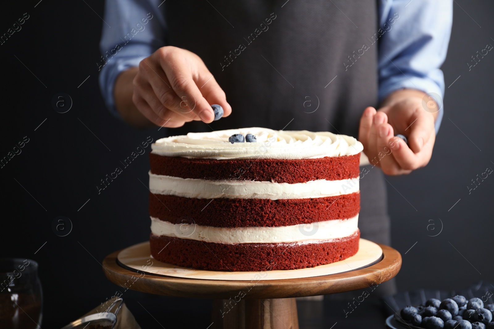 Photo of Woman decorating delicious homemade red velvet cake with blueberries at table