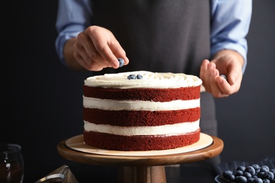 Woman decorating delicious homemade red velvet cake with blueberries at table