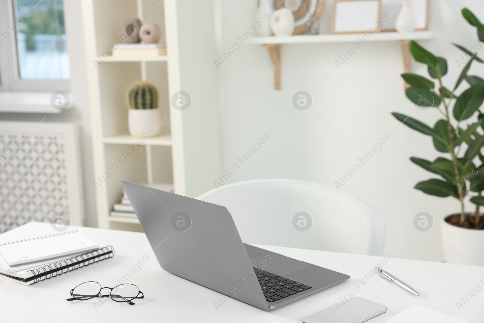 Photo of Home office. Laptop, glasses, notebooks, smartphone and pen on white desk indoors