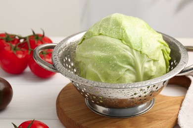 Photo of Wet cabbage in colander and tomatoes on white wooden table, closeup