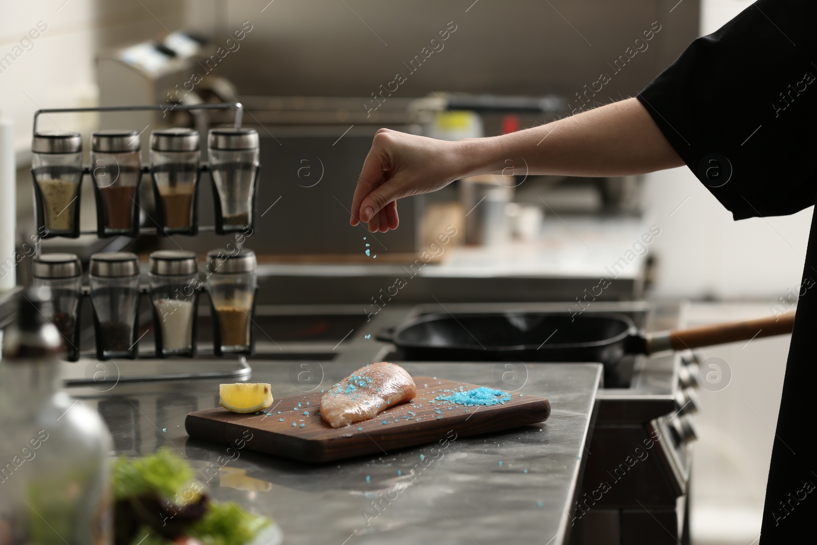 Photo of Female chef adding blue salt to raw chicken fillet in restaurant kitchen, closeup. Cooking food