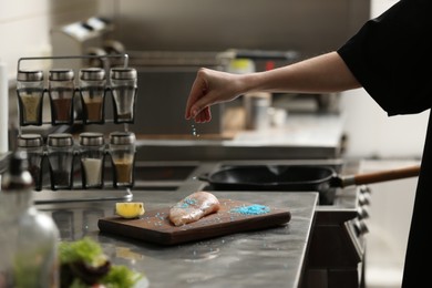 Photo of Female chef adding blue salt to raw chicken fillet in restaurant kitchen, closeup. Cooking food