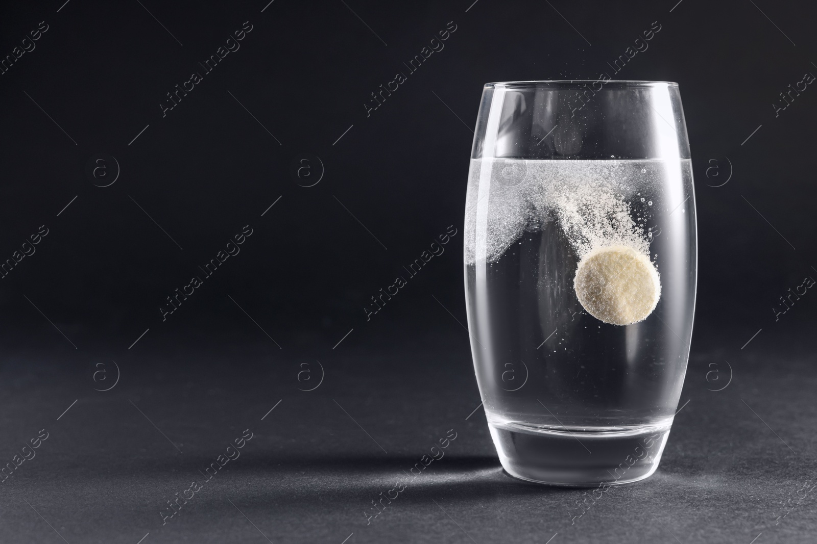 Photo of Effervescent pill dissolving in glass of water on grey table. Space for text