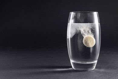 Effervescent pill dissolving in glass of water on grey table. Space for text