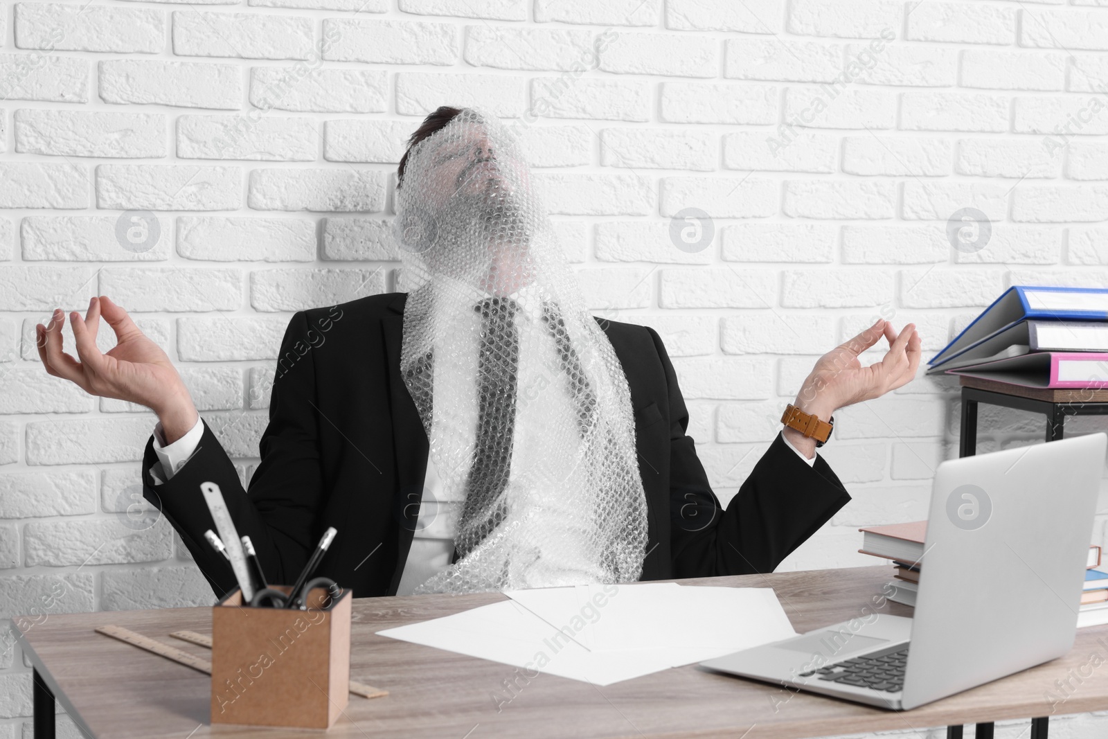 Photo of Businessman meditating with bubble wrap on his face at workplace