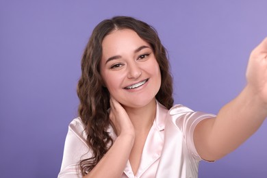 Smiling woman with braces taking selfie on violet background