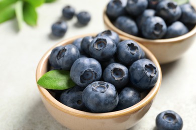 Tasty fresh blueberries in bowls on light grey table, closeup