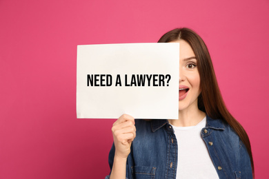 Emotional woman holding paper with text NEED A LAWYER? on pink background