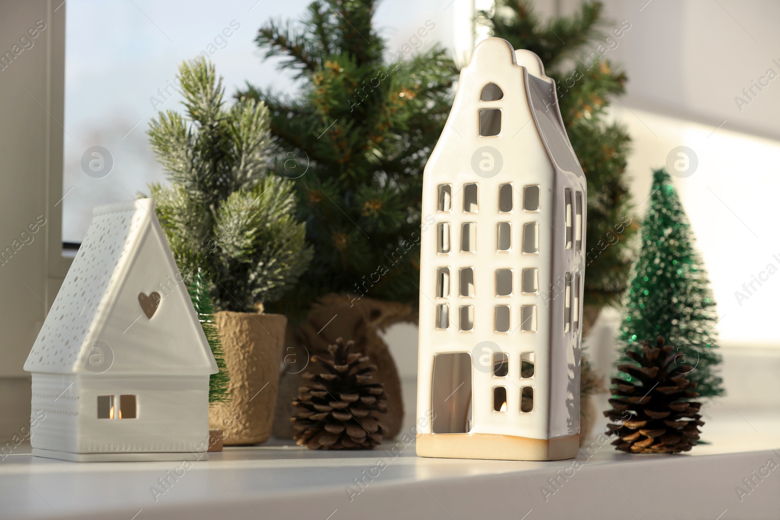 Photo of Beautiful house shaped candle holders and small fir trees on windowsill indoors