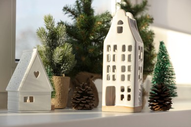 Beautiful house shaped candle holders and small fir trees on windowsill indoors