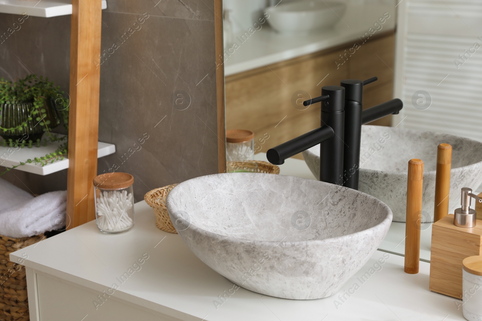 Photo of Stone vessel sink with faucet and toiletries on white countertop in bathroom