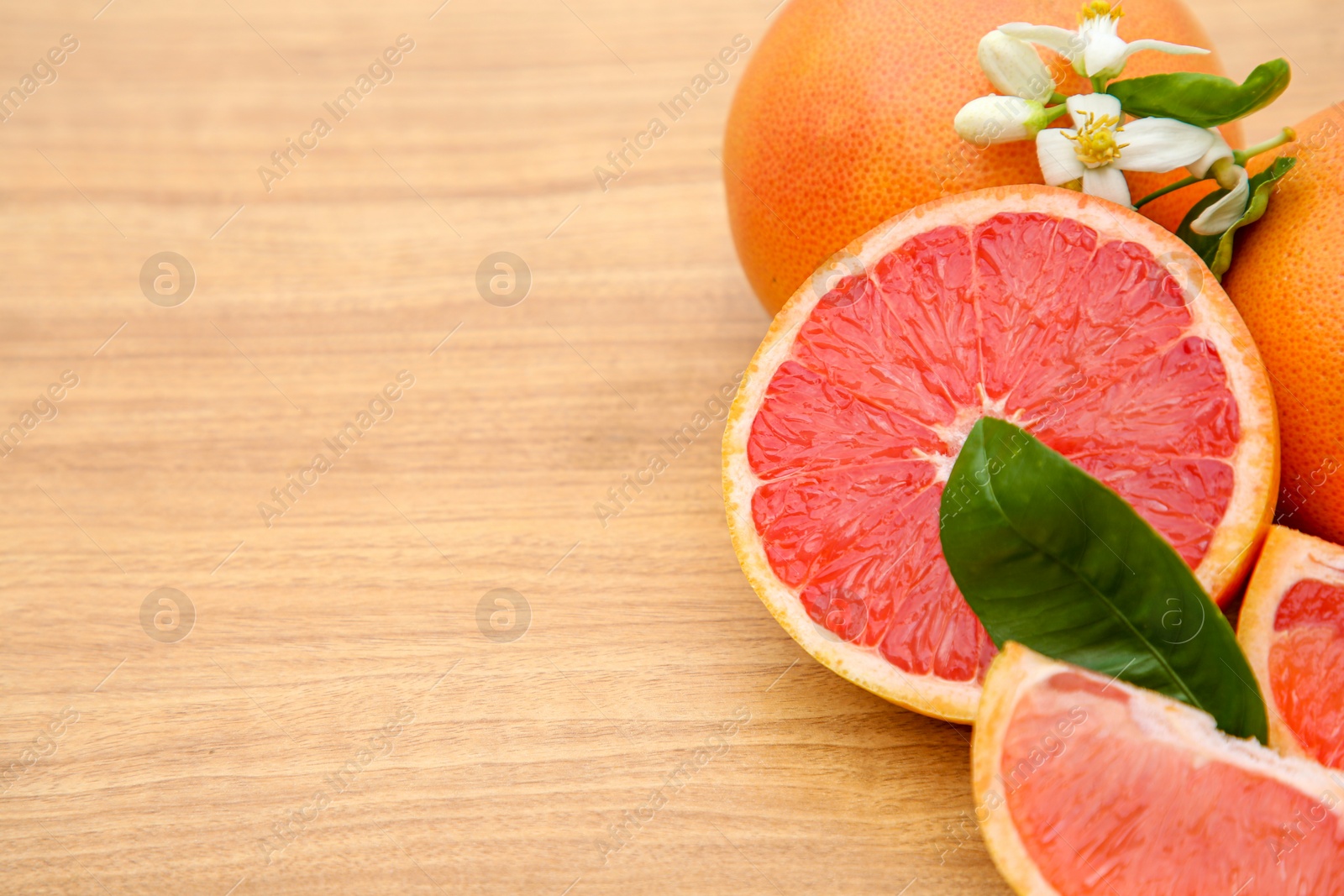 Photo of Fresh ripe grapefruits, flowers and green leaves on wooden table, closeup. Space for text