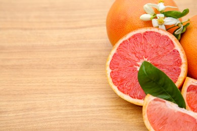 Photo of Fresh ripe grapefruits, flowers and green leaves on wooden table, closeup. Space for text