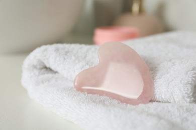 Photo of Rose quartz gua sha tool with soft towel on white table, closeup