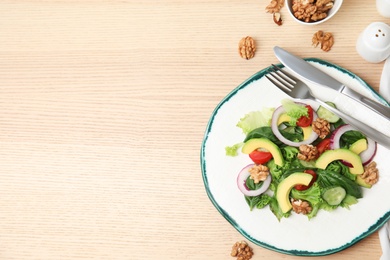 Delicious avocado salad with walnuts on wooden table, flat lay. Space for text