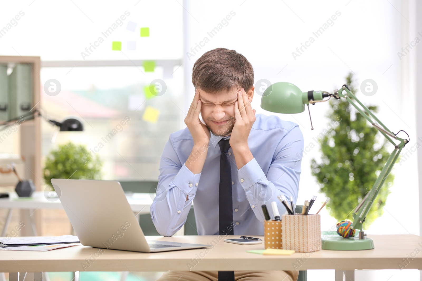 Photo of Young man suffering from headache in office