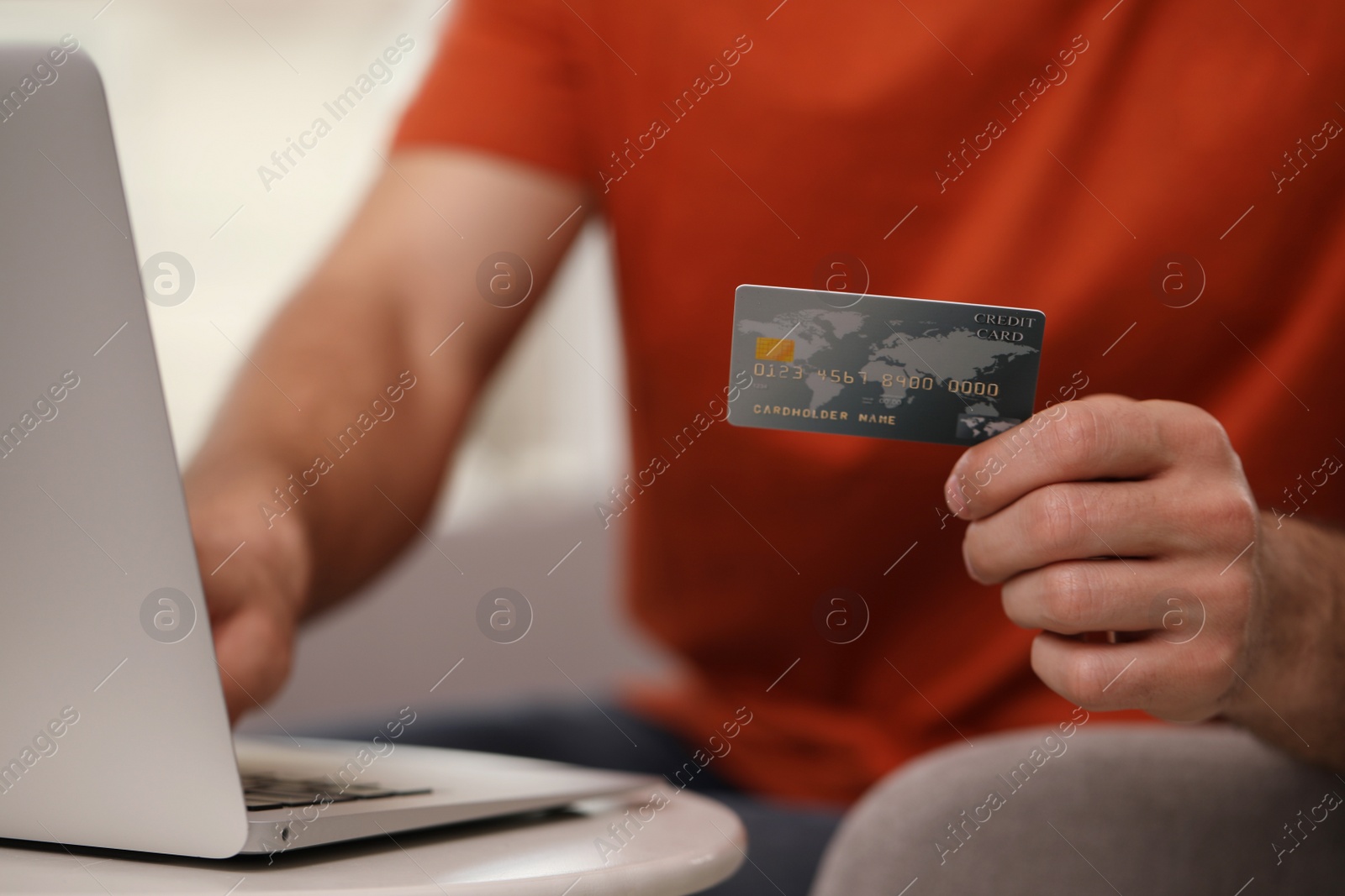 Photo of Man using laptop and credit card for online payment at table indoors, closeup