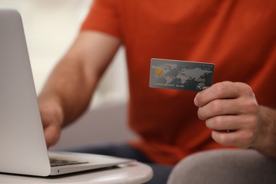 Photo of Man using laptop and credit card for online payment at table indoors, closeup