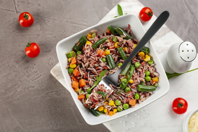 Photo of Tasty brown rice with vegetables served on grey table, flat lay