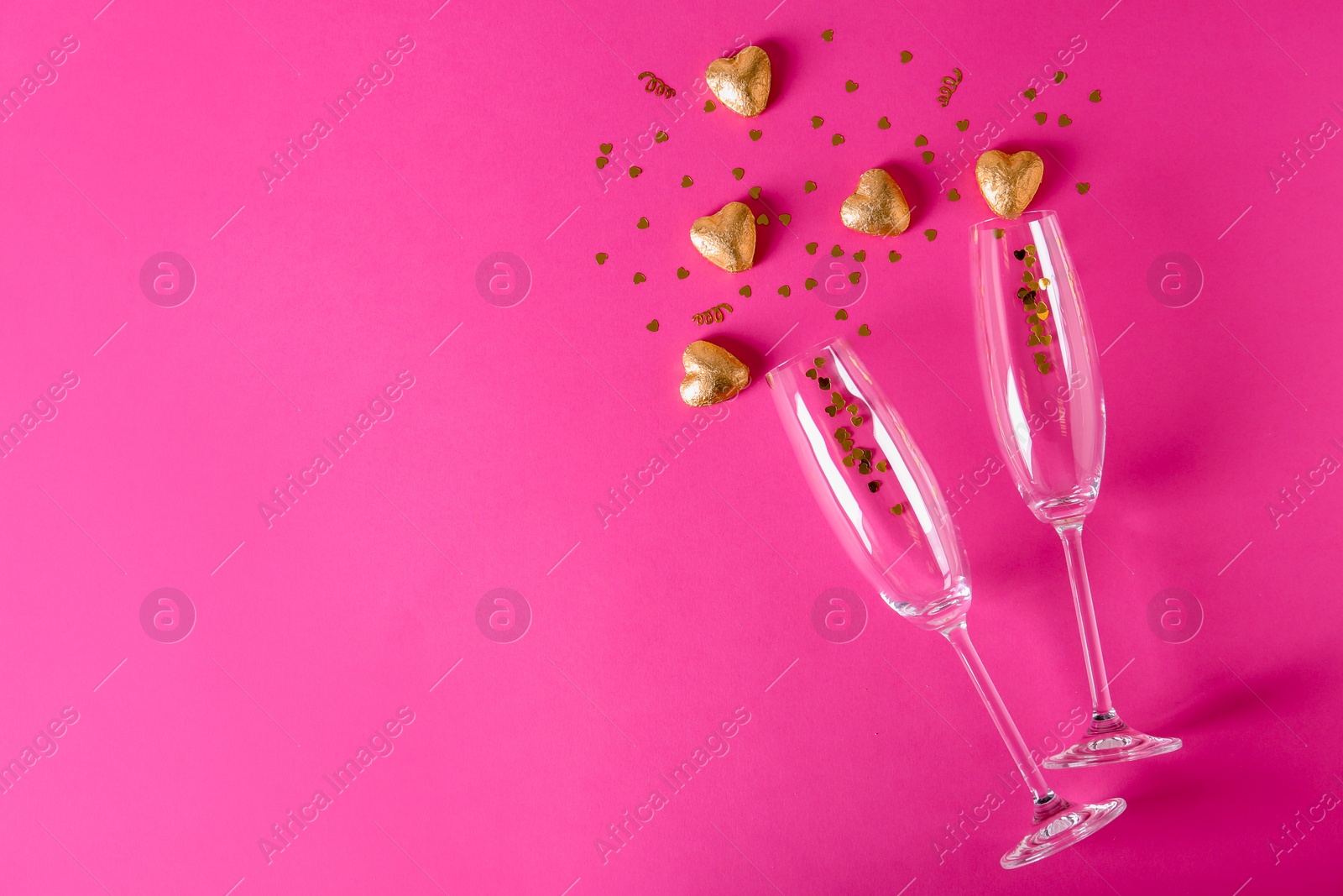 Photo of Champagne glasses and heart shaped candies in golden foil on color background, top view