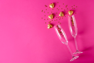 Champagne glasses and heart shaped candies in golden foil on color background, top view