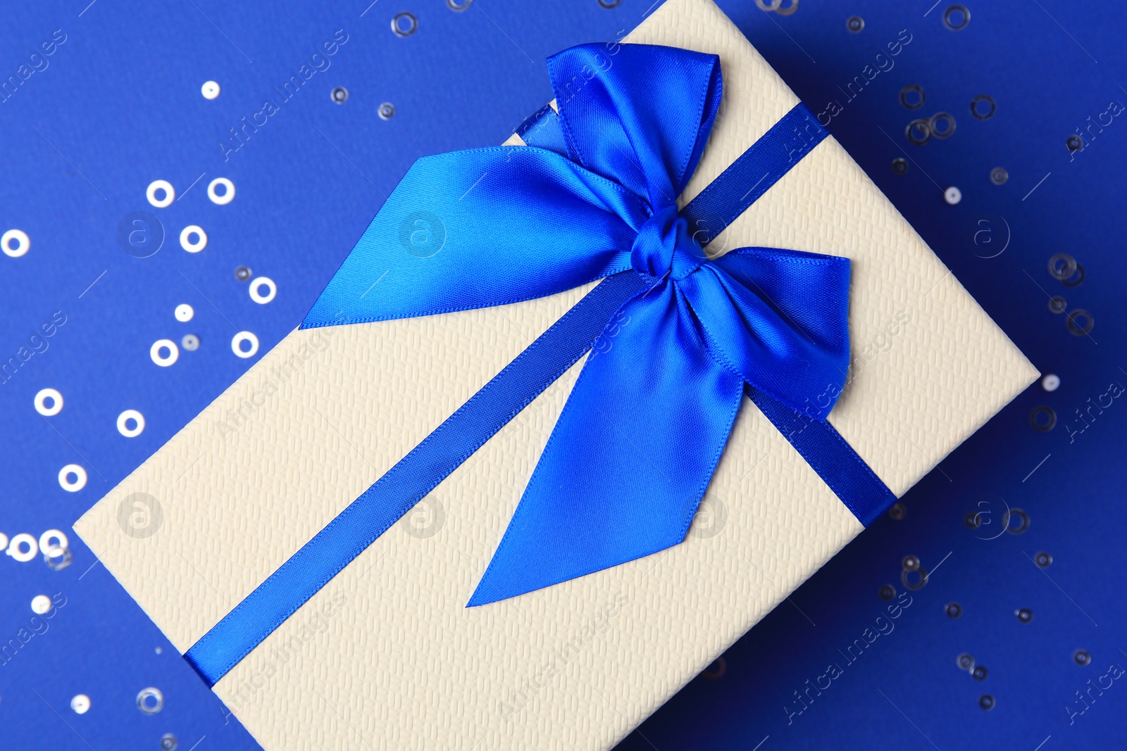 Photo of Beautiful gift box with bow and confetti on blue background, top view