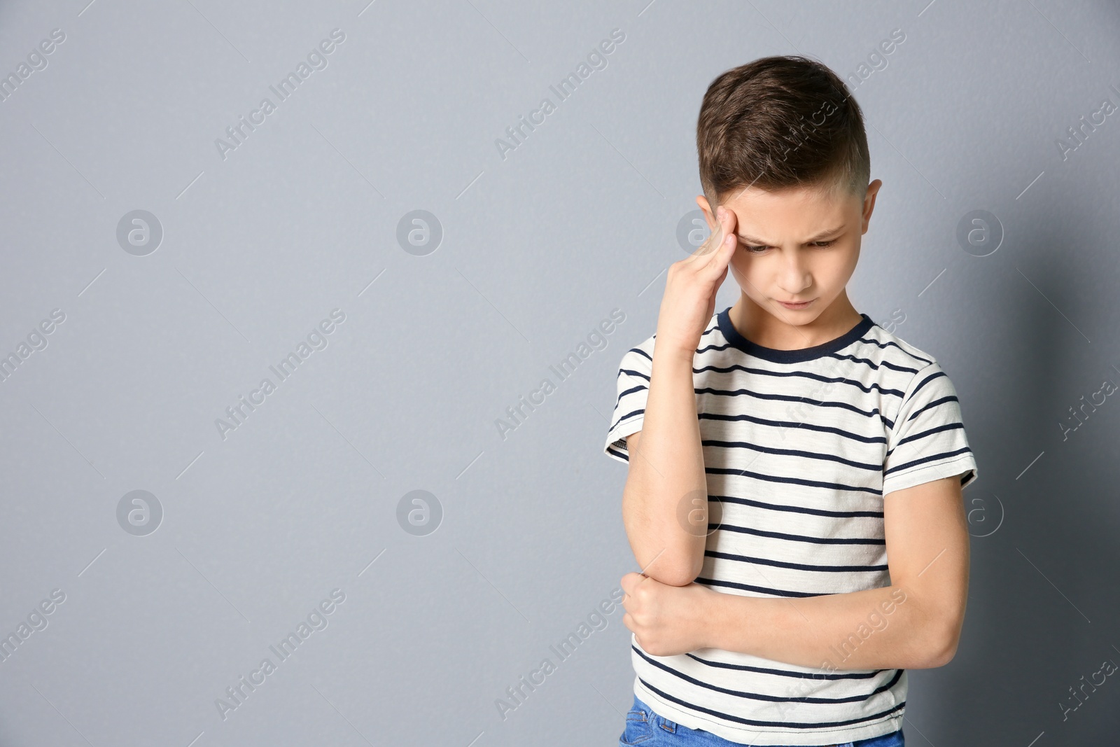 Photo of Little boy suffering from headache on grey background