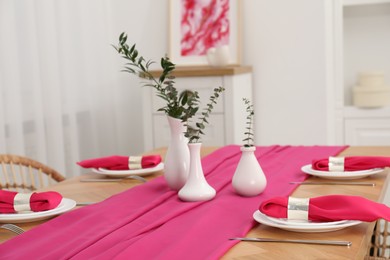 Beautiful table setting and vases with green branches in dining room