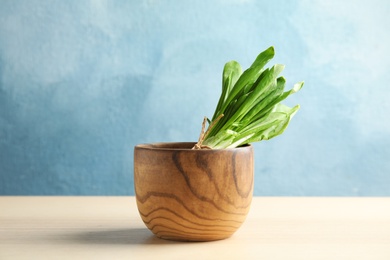 Wooden bowl with bunch of wild garlic or ramson on table against color background