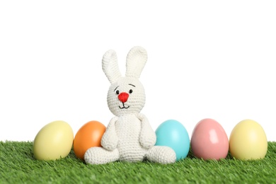 Photo of Cute Easter bunny toy and dyed eggs on green grass against white background